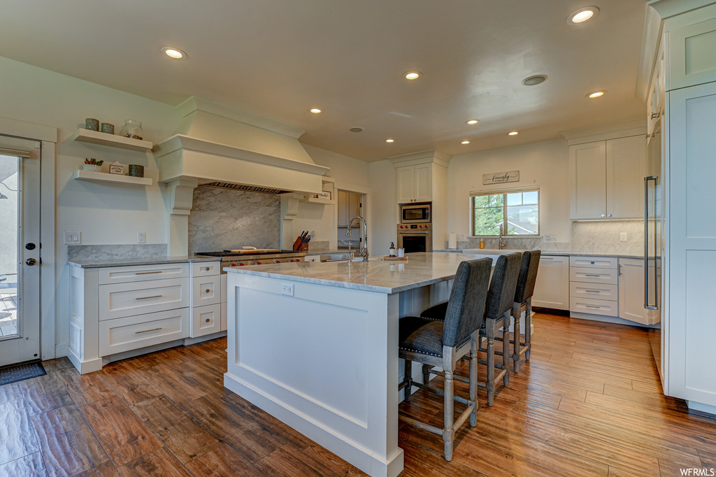 Kitchen with tasteful backsplash, light stone counters, a breakfast bar, white cabinets, and a center island with sink