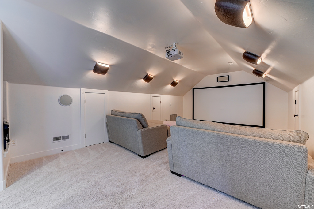 Home theater room with lofted ceiling and light carpet