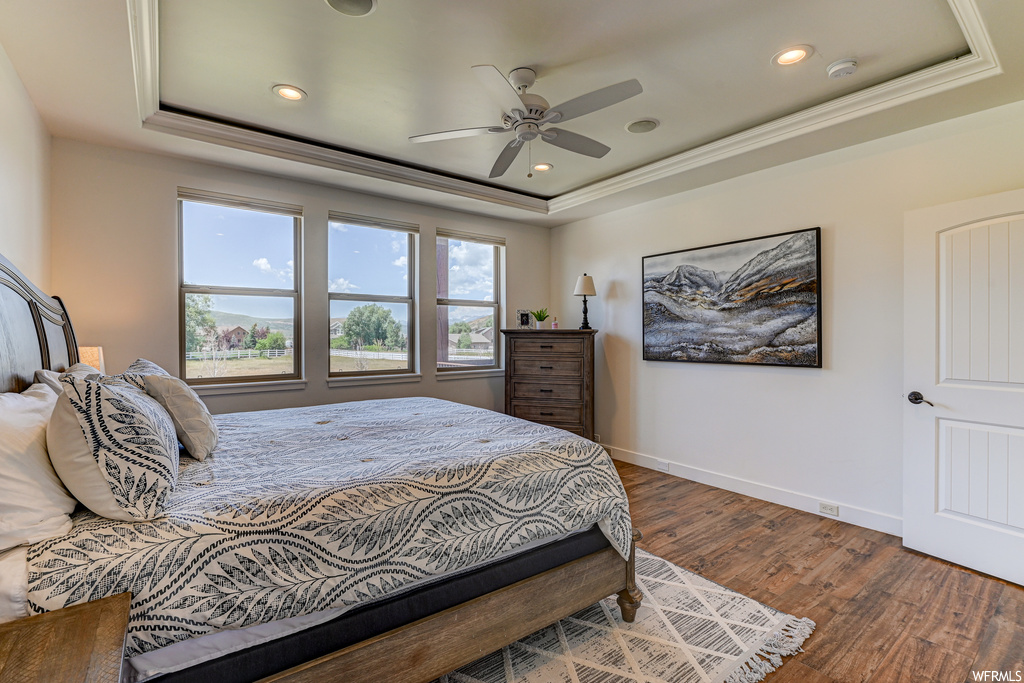 Bedroom featuring dark wood-type flooring, a raised ceiling, ceiling fan, and crown molding