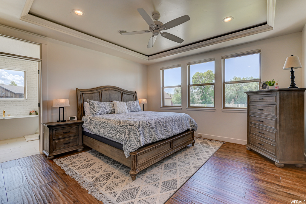 Bedroom with multiple windows, a tray ceiling, dark wood-type flooring, and ceiling fan