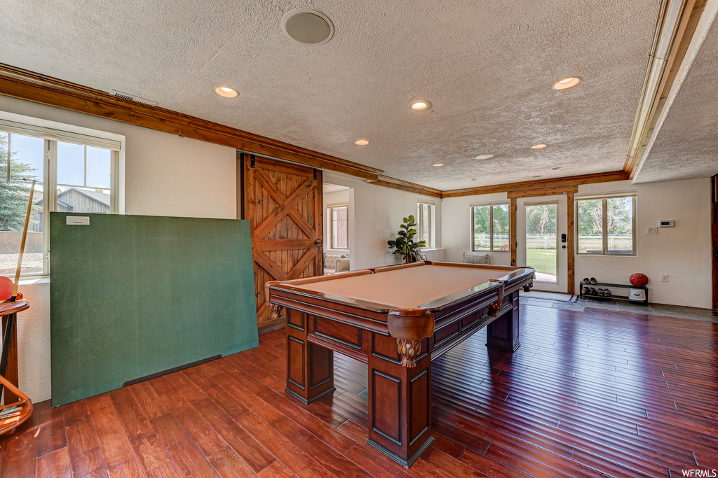 Game room featuring billiards, a barn door, dark hardwood / wood-style flooring, and crown molding