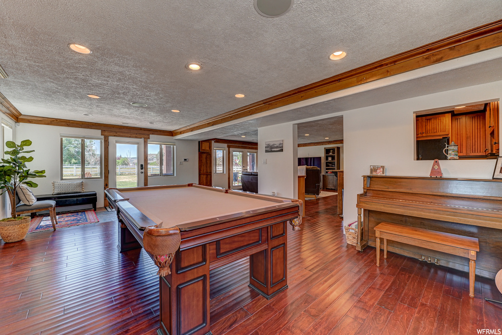 Game room with dark wood-type flooring, a textured ceiling, ornamental molding, and billiards
