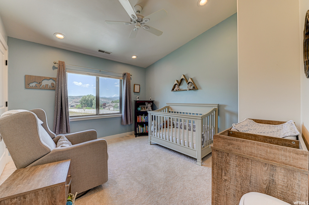 Carpeted bedroom featuring ceiling fan, a nursery area, and vaulted ceiling