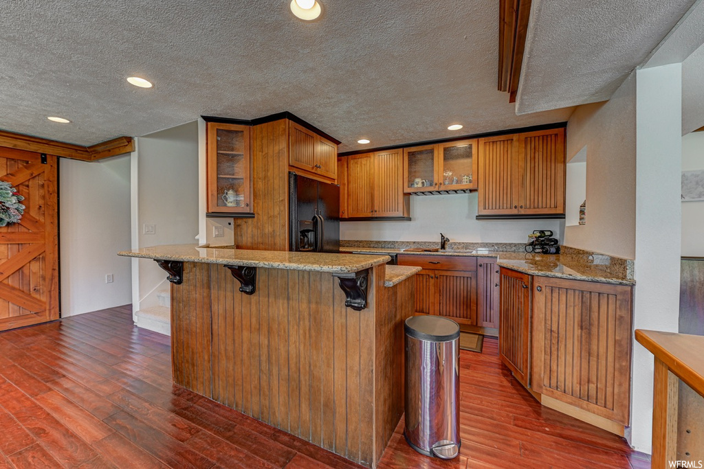 Kitchen featuring dark hardwood / wood-style flooring, kitchen peninsula, black refrigerator with ice dispenser, and a textured ceiling