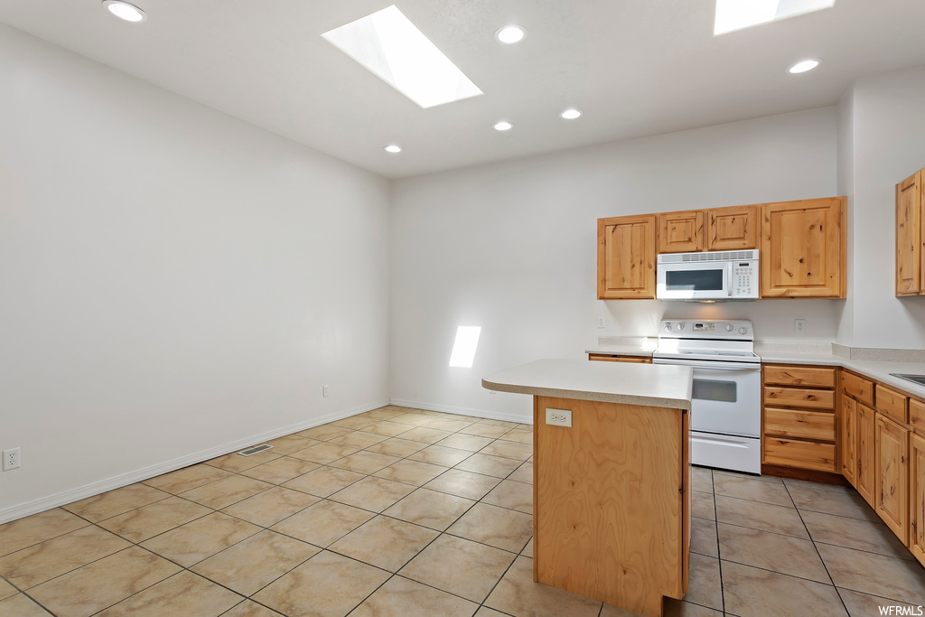 Kitchen featuring white appliances, light tile floors, brown cabinets, light countertops, and a skylight