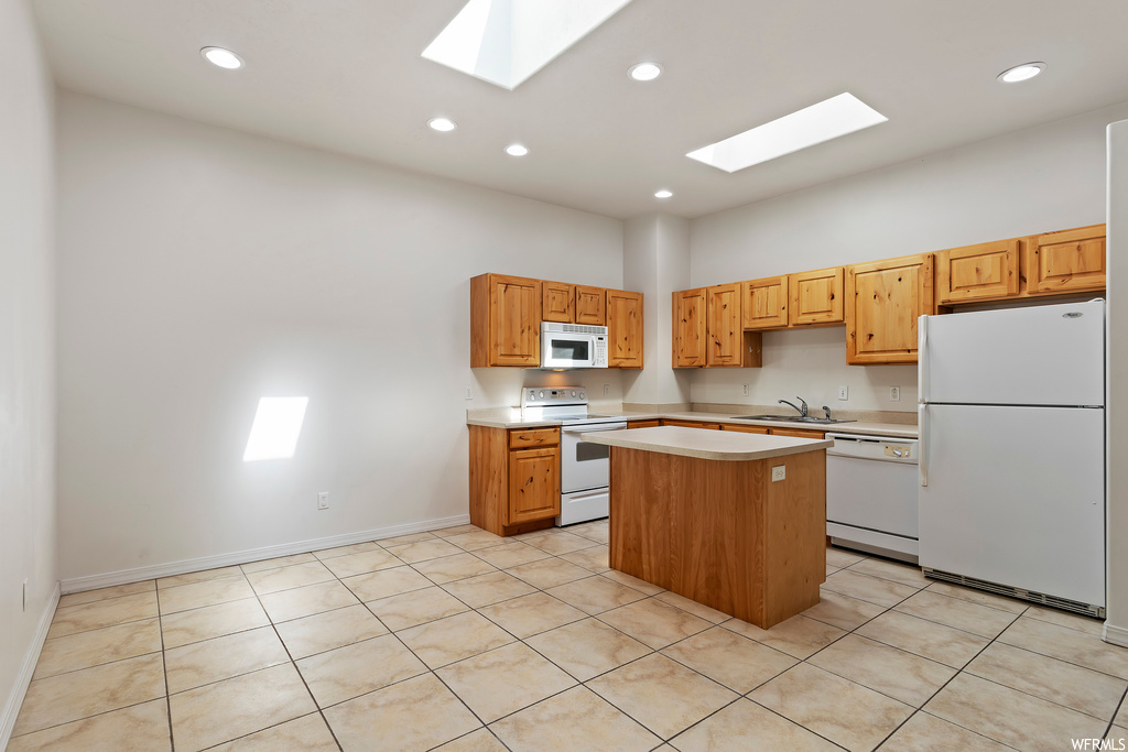 Kitchen with brown cabinets, light tile floors, white appliances, a skylight, and light countertops