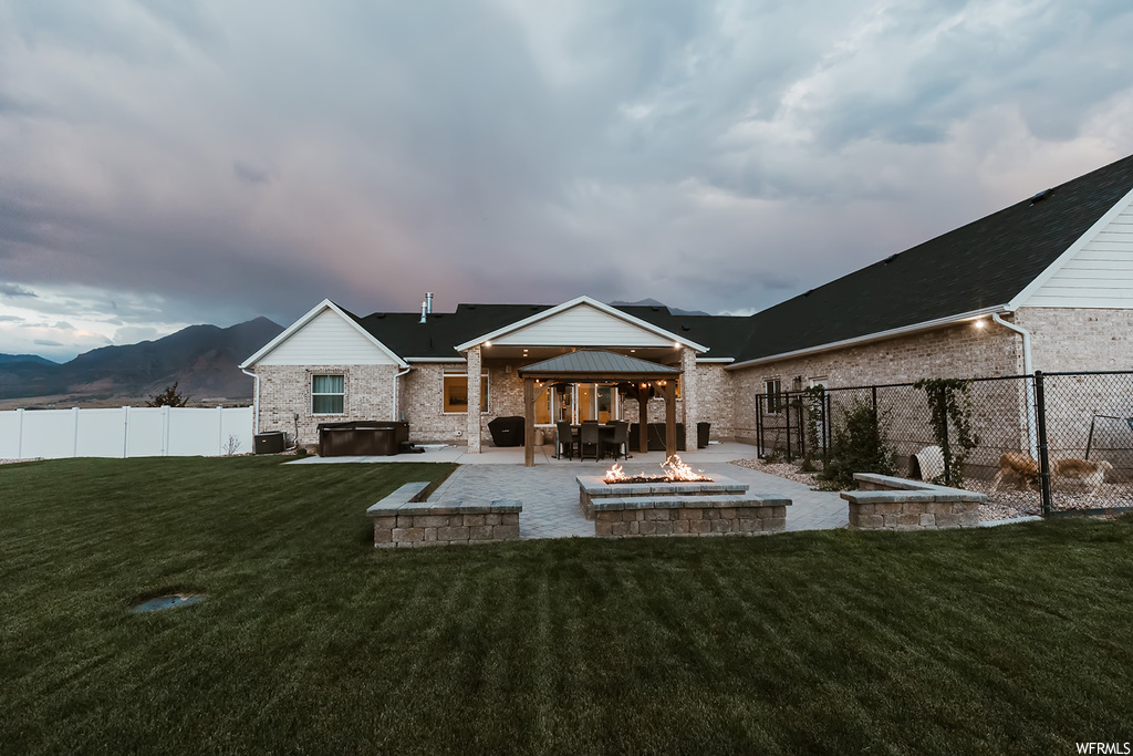 Back of property featuring a firepit, a patio, a lawn, and a mountain view