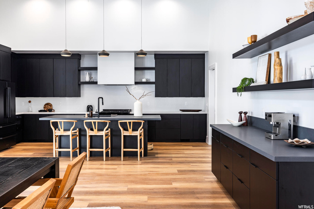 Kitchen with dark brown cabinets, backsplash, dark countertops, light hardwood flooring, and a center island
