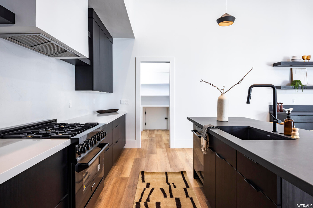 Kitchen featuring dark brown cabinets, premium range hood, high end stainless steel range, light countertops, light hardwood flooring, and pendant lighting