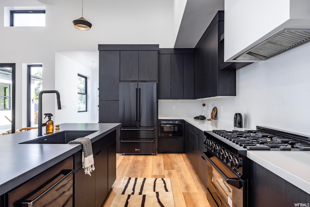 Kitchen with dark brown cabinets, hanging light fixtures, high end appliances, custom range hood, light countertops, and light hardwood floors