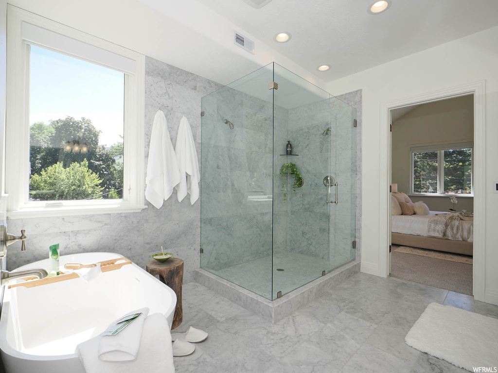 Bathroom with separate shower and tub, a wealth of natural light, tile walls, and light tile flooring