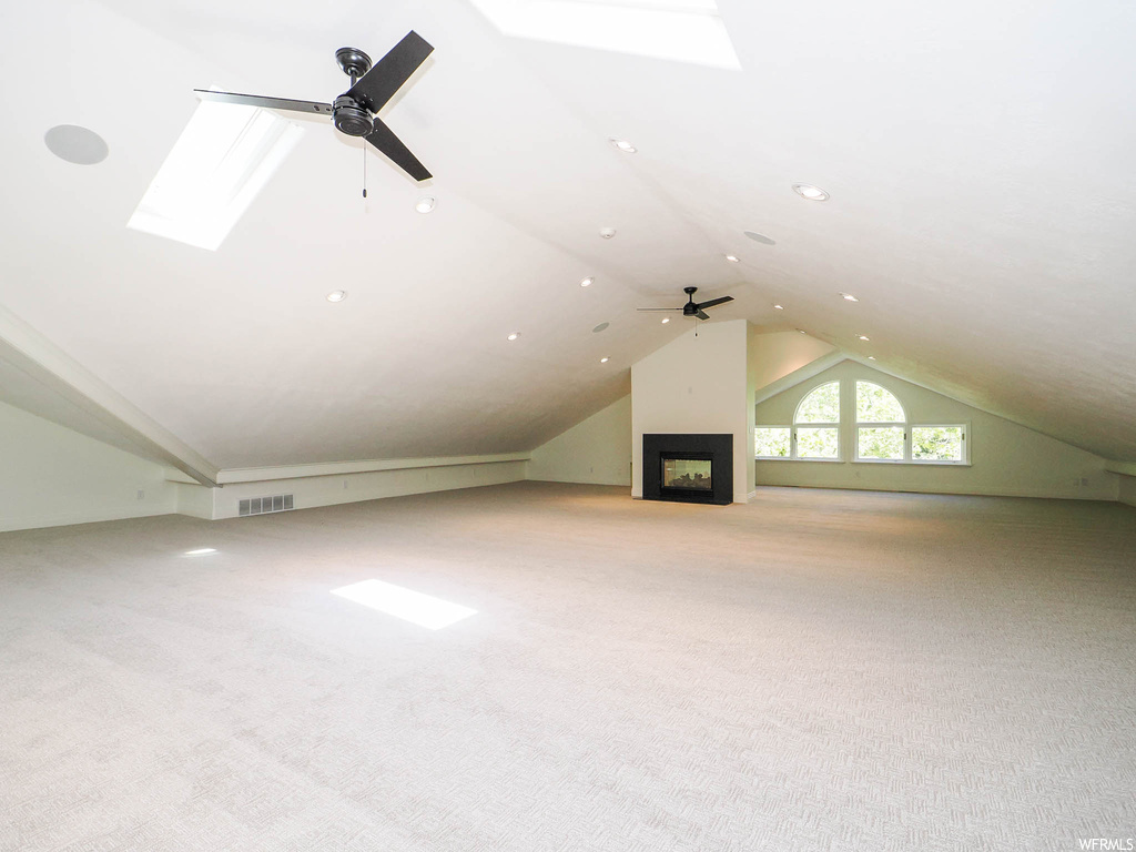Additional living space featuring lofted ceiling with skylight, ceiling fan, and light carpet