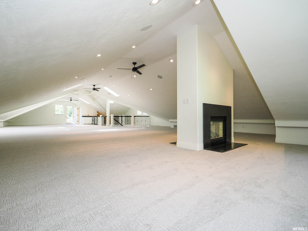 Additional living space featuring a fireplace, ceiling fan, light carpet, and lofted ceiling