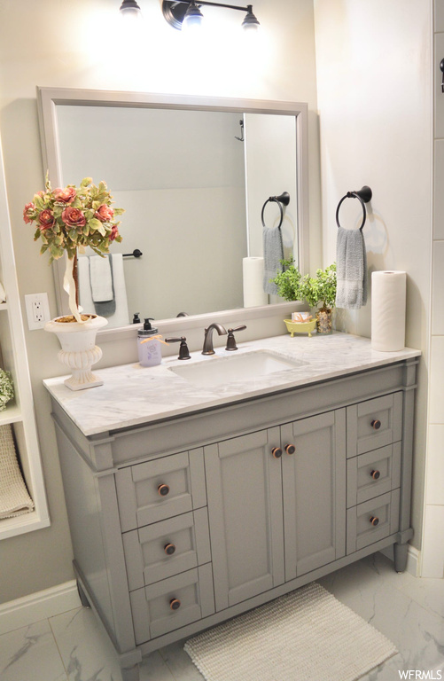 Bathroom featuring vanity with extensive cabinet space, mirror, and light tile floors
