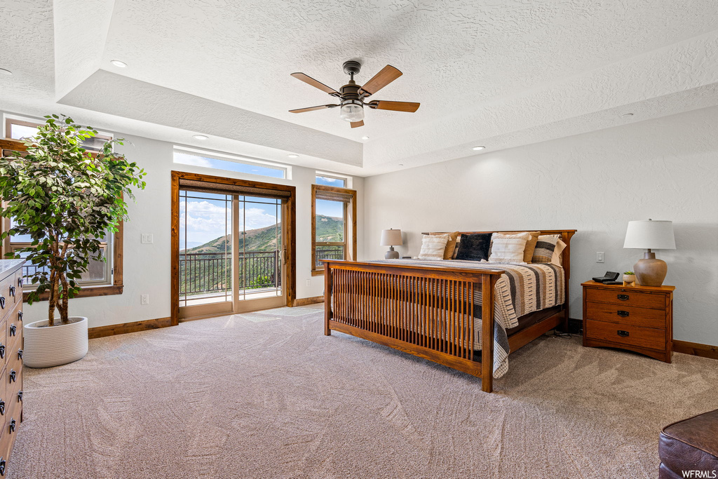 Bedroom featuring a textured ceiling, a raised ceiling, ceiling fan, and light carpet