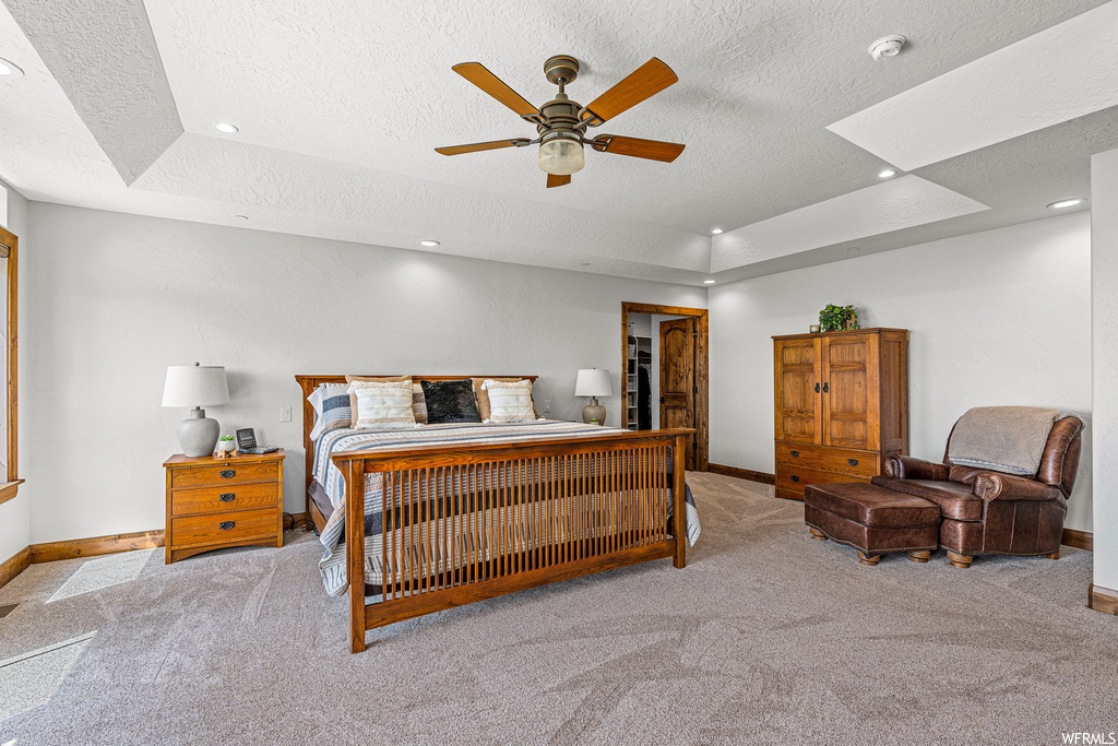 Carpeted bedroom featuring ceiling fan, a tray ceiling, and a textured ceiling