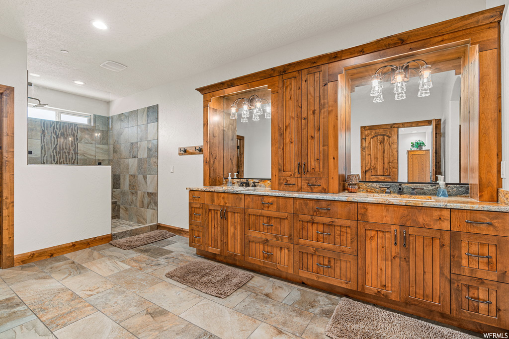 Bathroom with a shower with door, light tile floors, mirror, and dual bowl vanity