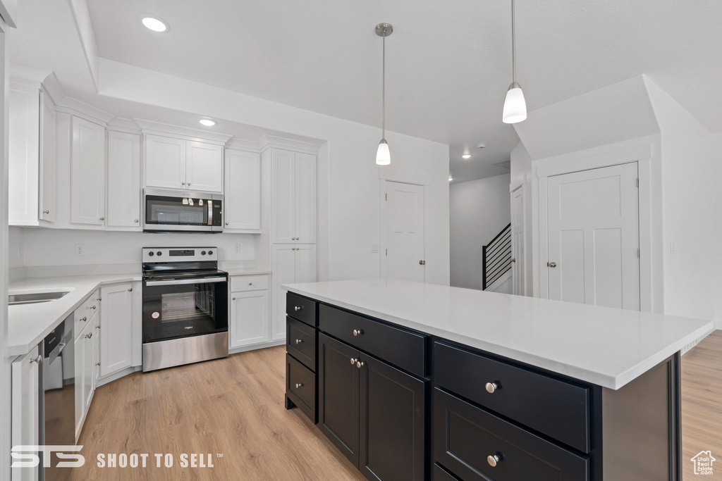 Kitchen featuring decorative light fixtures, white cabinets, stainless steel appliances, and light hardwood / wood-style floors