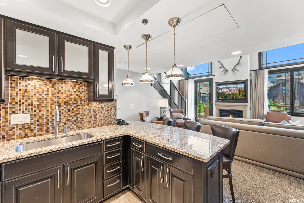 Kitchen featuring dark brown cabinets, backsplash, a tray ceiling, light stone countertops, pendant lighting, and carpet flooring
