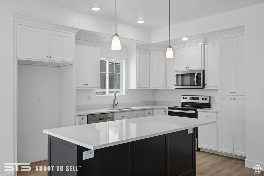 Kitchen featuring white cabinets, a kitchen island, decorative light fixtures, and stainless steel appliances
