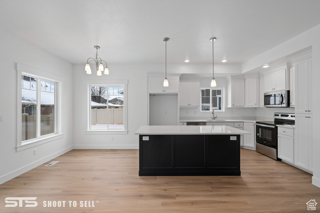Kitchen with appliances with stainless steel finishes, white cabinets, a notable chandelier, and light hardwood / wood-style floors