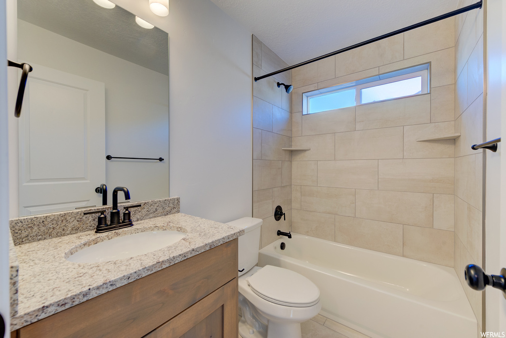 Full bathroom featuring toilet, a textured ceiling, tiled shower / bath, and oversized vanity