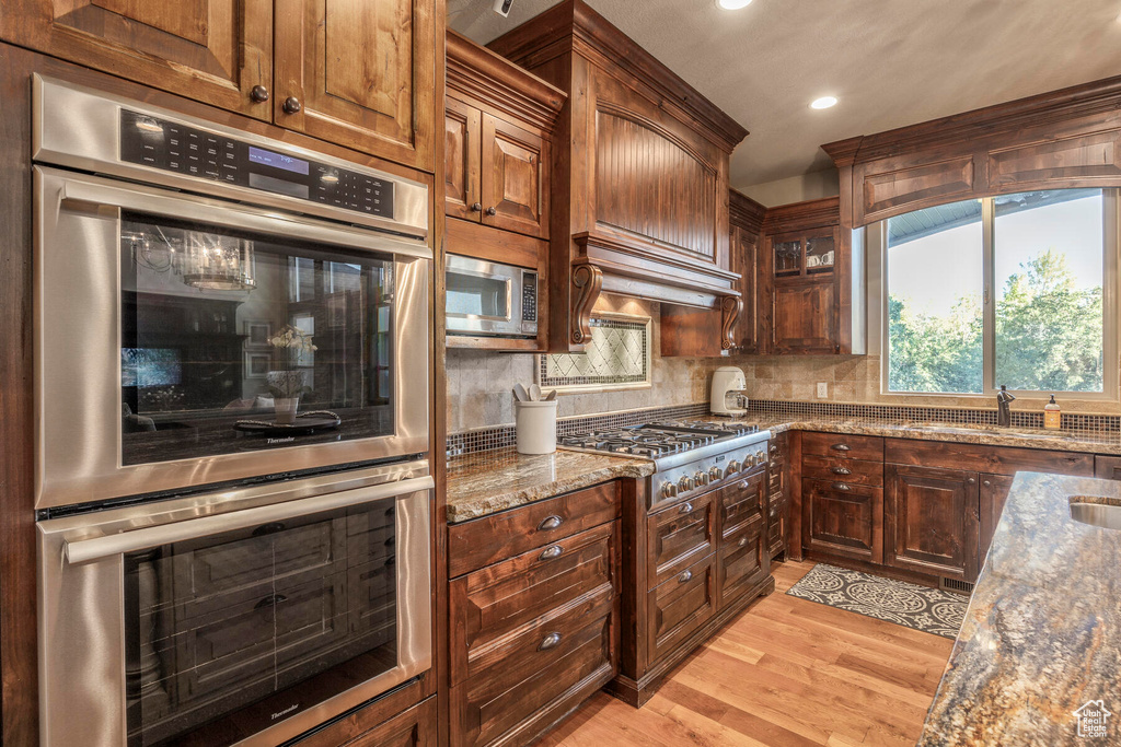 Kitchen featuring light wood-type flooring, stone countertops, backsplash, sink, and stainless steel appliances
