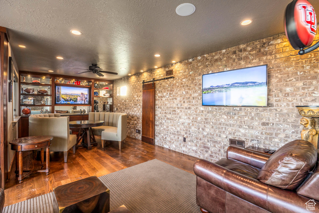 Living room featuring a barn door, brick wall, dark wood-type flooring, and ceiling fan