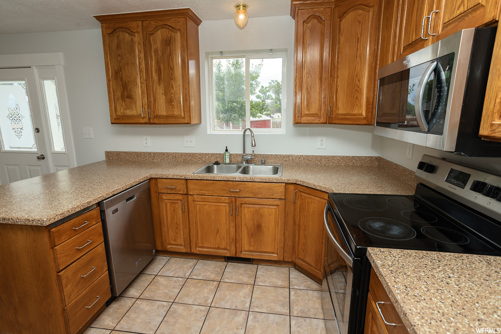 Kitchen with appliances with stainless steel finishes, light countertops, light tile floors, and brown cabinets