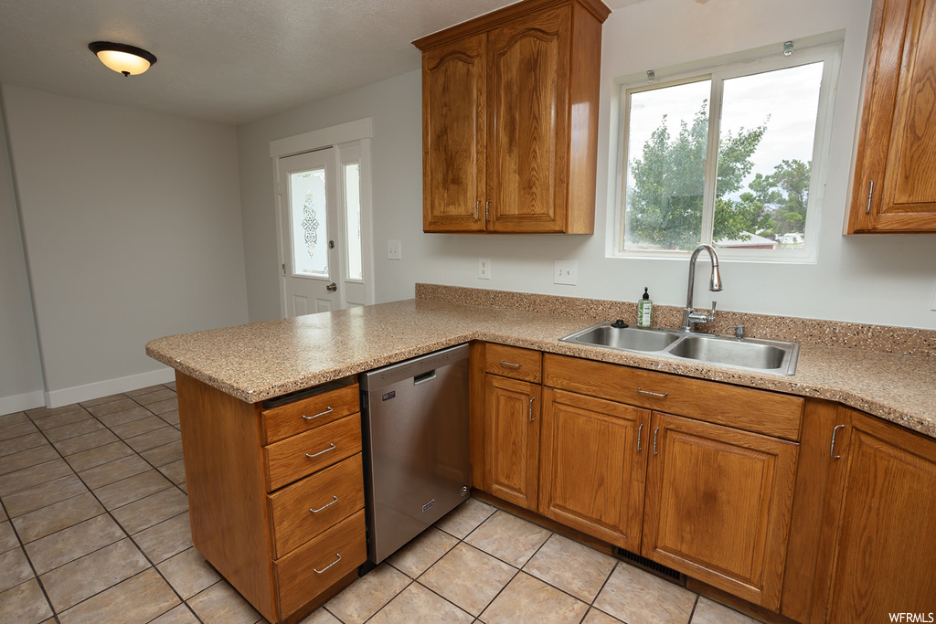 Kitchen with brown cabinets, light tile floors, plenty of natural light, stainless steel dishwasher, and light countertops