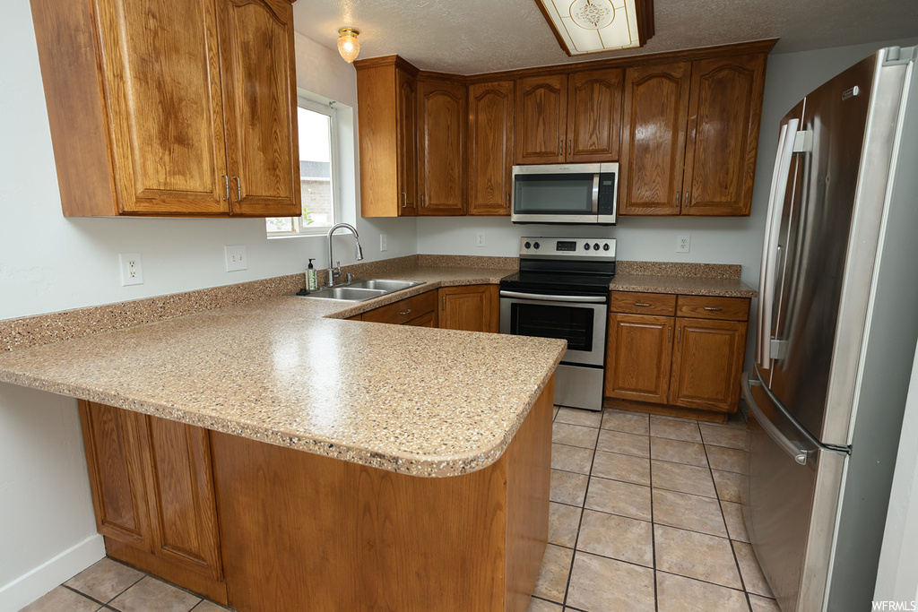 Kitchen featuring appliances with stainless steel finishes, light countertops, light tile floors, and brown cabinets