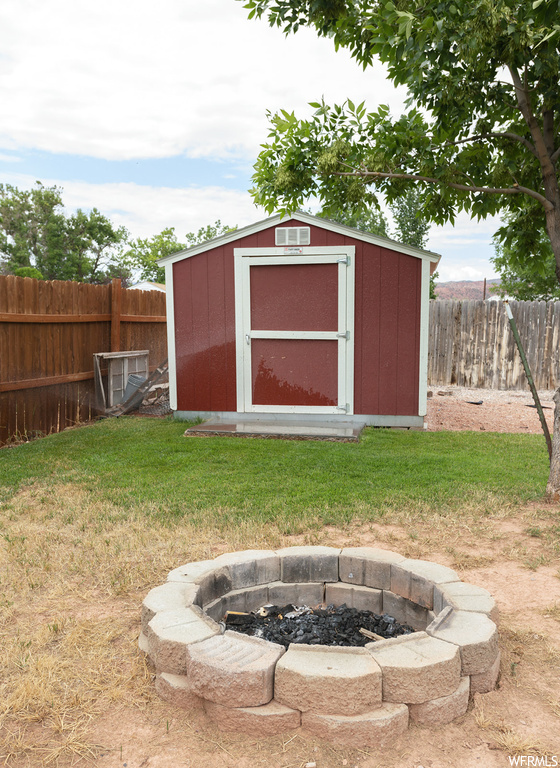 View of outdoor structure featuring a storage unit, a firepit, and a lawn