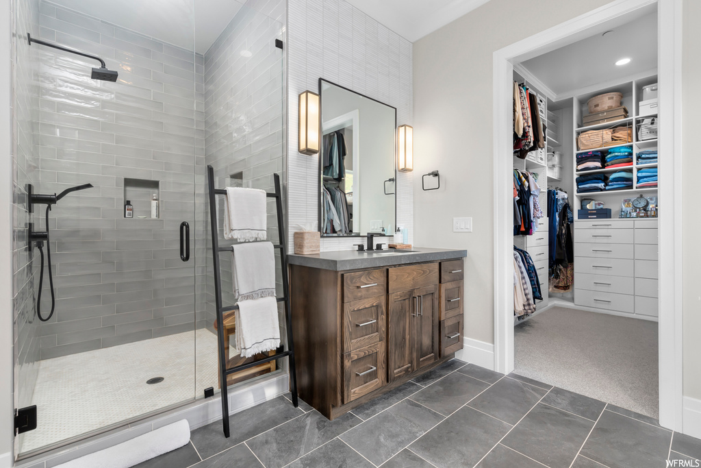 Bathroom featuring light tile floors, vanity with extensive cabinet space, a shower with shower door, and mirror