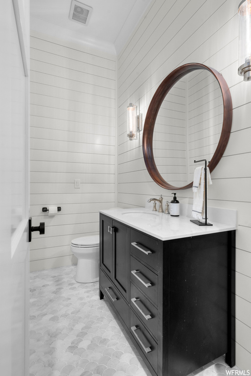 Bathroom featuring light tile floors, wooden walls, vanity, and mirror