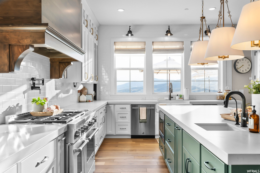 Kitchen featuring white cabinets, light hardwood flooring, appliances with stainless steel finishes, hanging light fixtures, light countertops, and backsplash