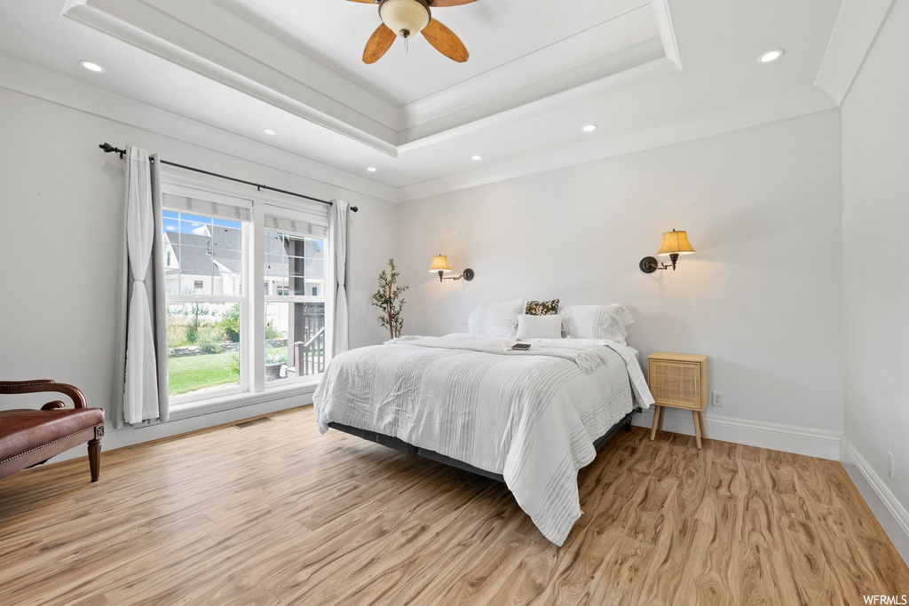 Hardwood floored bedroom featuring crown molding, a raised ceiling, and ceiling fan