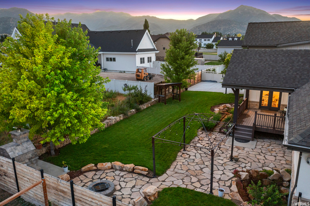 Yard at dusk with a deck with mountain view, an outdoor firepit, and a patio
