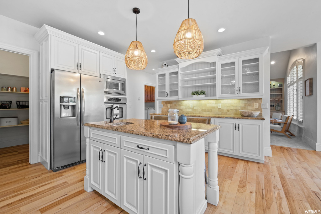 Kitchen featuring pendant lighting, a center island with sink, light parquet floors, appliances with stainless steel finishes, light granite-like countertops, backsplash, and white cabinetry