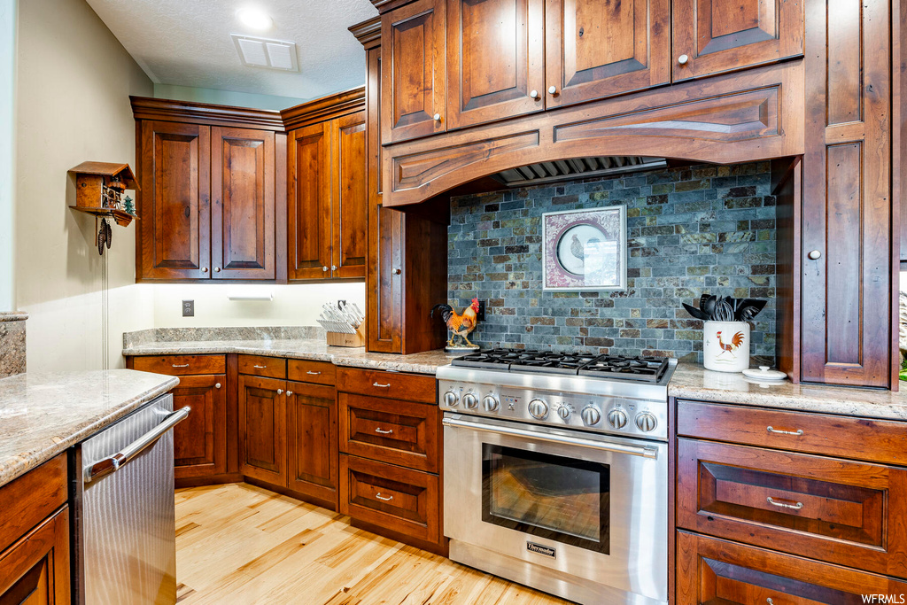 Kitchen featuring backsplash, brown cabinets, light countertops, light hardwood flooring, and high end stainless steel range oven