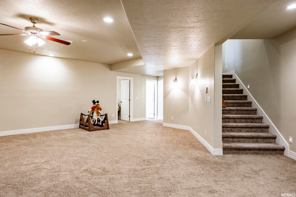 Interior space with a textured ceiling, ceiling fan, and light carpet