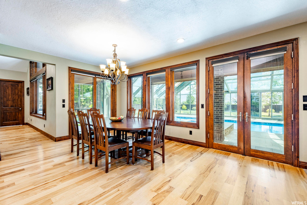 Dining room featuring light hardwood flooring, a notable chandelier, a textured ceiling, a wealth of natural light, and french doors