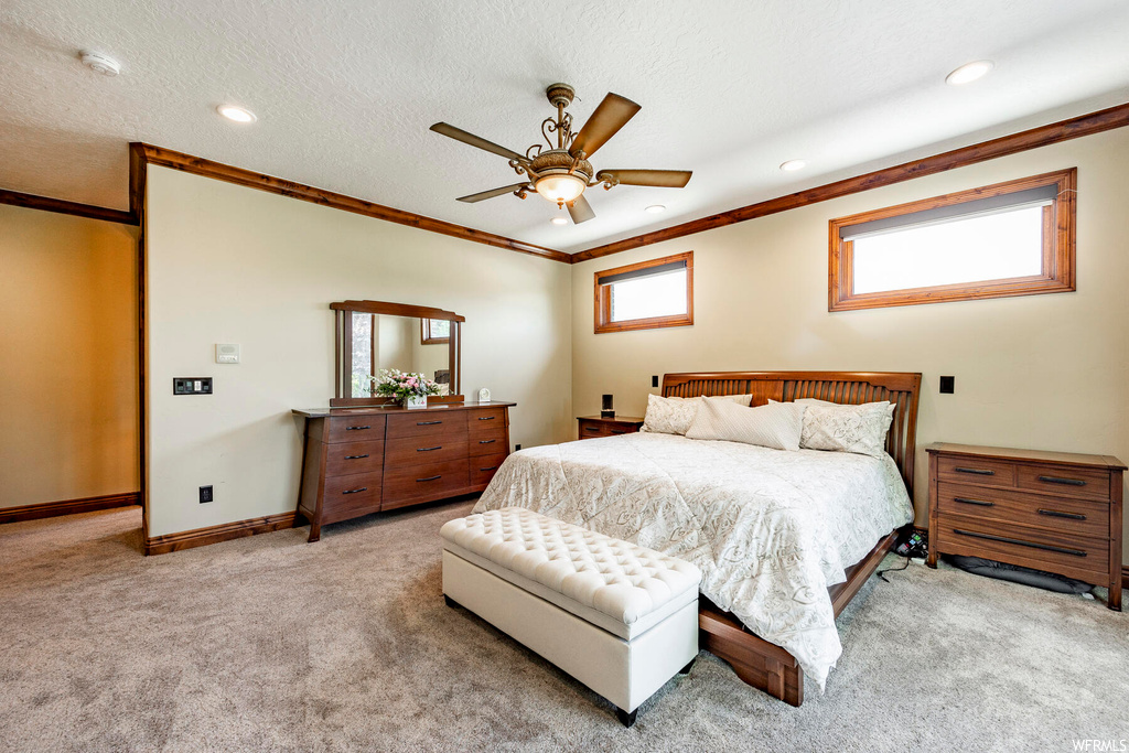 Carpeted bedroom featuring a textured ceiling, ceiling fan, multiple windows, and ornamental molding