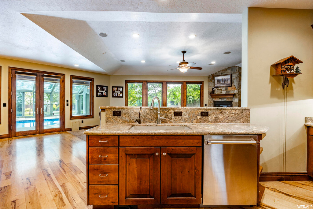 Kitchen featuring light stone counters, light hardwood flooring, lofted ceiling, a textured ceiling, french doors, stainless steel dishwasher, and ceiling fan