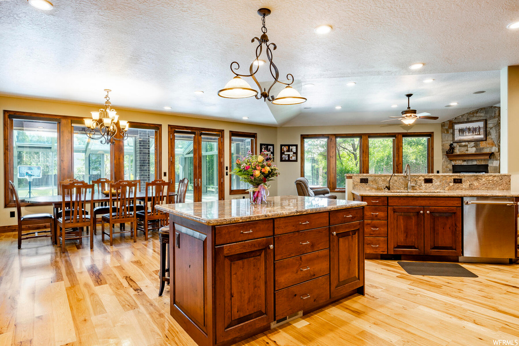 Kitchen featuring lofted ceiling, ceiling fan with notable chandelier, a textured ceiling, light stone countertops, light hardwood flooring, a kitchen island with sink, and stainless steel dishwasher