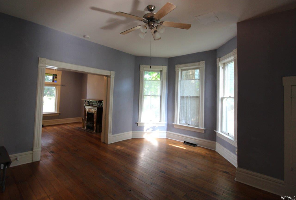 Spare room featuring dark hardwood floors, ceiling fan, and a fireplace