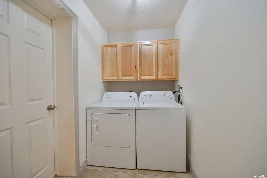 Washroom with light tile flooring and washing machine and dryer