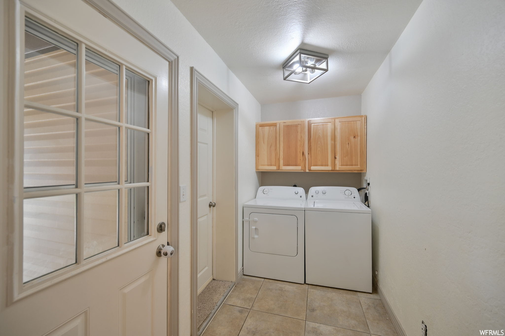 Clothes washing area with separate washer and dryer, a textured ceiling, and light tile floors