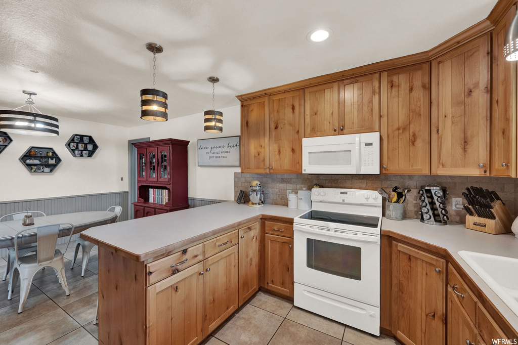 Kitchen with pendant lighting, brown cabinets, light tile floors, white appliances, light countertops, and backsplash