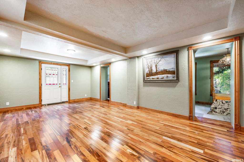 Empty room featuring a tray ceiling, a textured ceiling, and light hardwood flooring