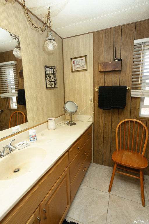 Bathroom featuring large vanity, mirror, light tile floors, and wooden walls